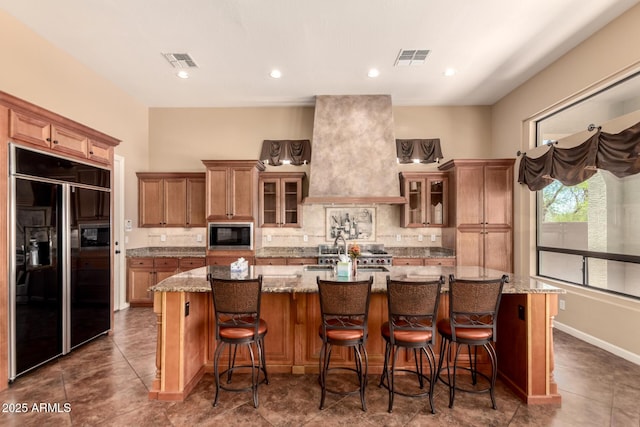 kitchen featuring built in appliances, a spacious island, decorative backsplash, glass insert cabinets, and light stone countertops