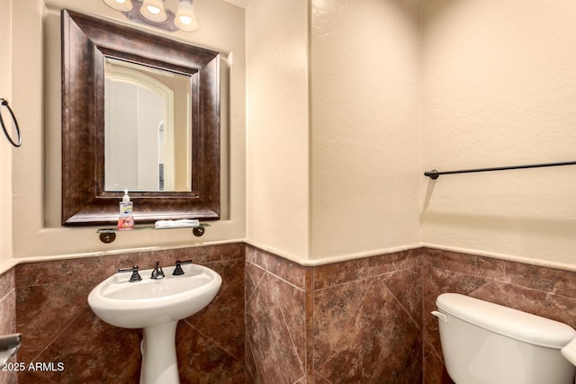 half bathroom with tile walls, a wainscoted wall, and toilet