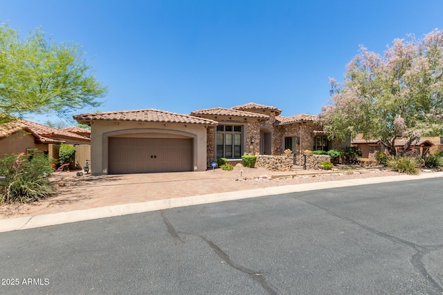 mediterranean / spanish house with stucco siding, an attached garage, driveway, and a tiled roof