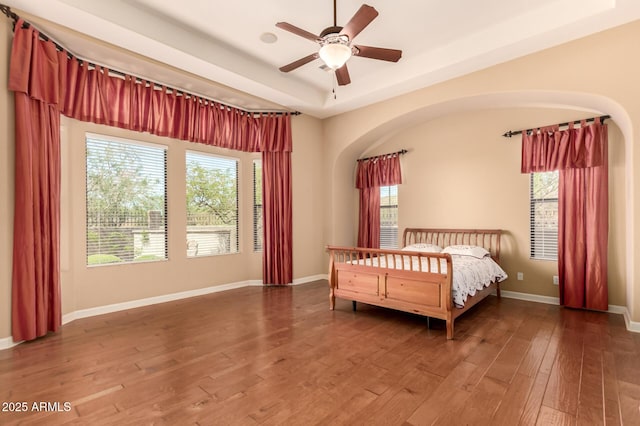 bedroom featuring hardwood / wood-style flooring, baseboards, a tray ceiling, and ceiling fan