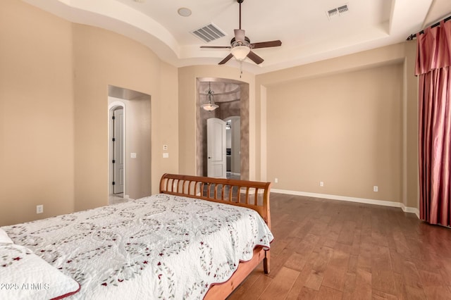 bedroom with arched walkways, wood-type flooring, baseboards, ceiling fan, and a raised ceiling