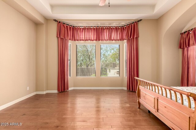 unfurnished bedroom with hardwood / wood-style floors, baseboards, arched walkways, and ceiling fan