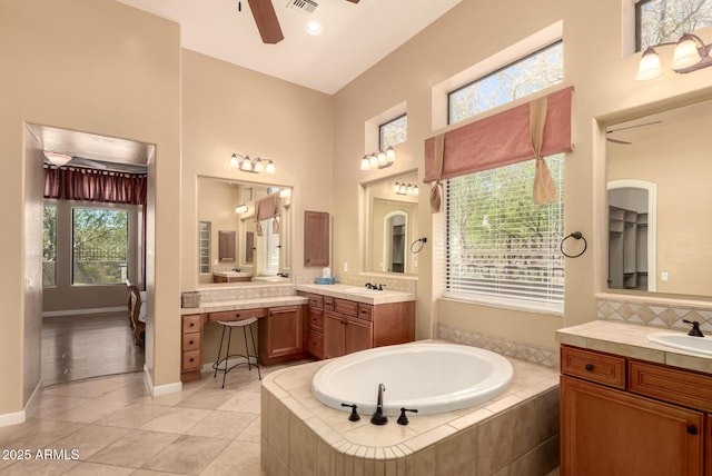 bathroom featuring a ceiling fan, a bath, tile patterned floors, two vanities, and backsplash