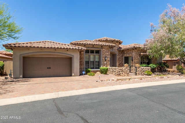 mediterranean / spanish-style house featuring stucco siding, an attached garage, a tiled roof, decorative driveway, and stone siding