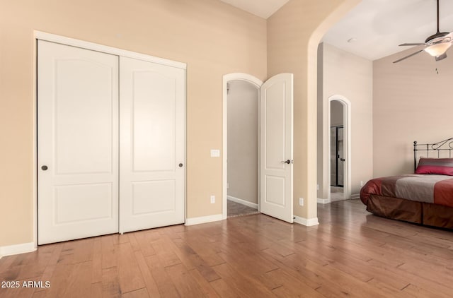 bedroom with arched walkways, a high ceiling, wood finished floors, a closet, and baseboards