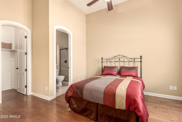 bedroom featuring hardwood / wood-style flooring, baseboards, ensuite bath, and lofted ceiling