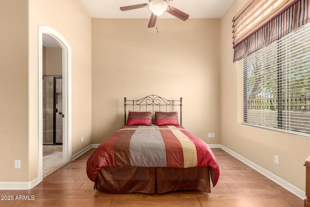 bedroom featuring wood finished floors, baseboards, ensuite bath, and arched walkways