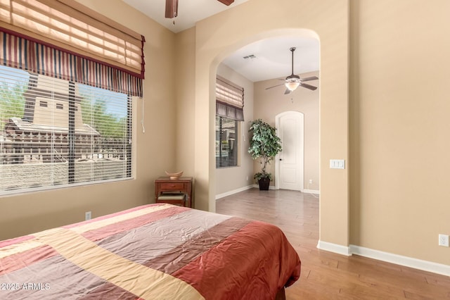 bedroom featuring arched walkways, wood finished floors, baseboards, and a ceiling fan