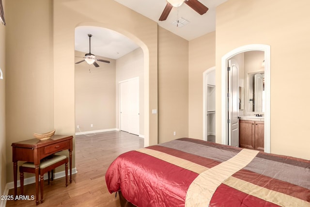 bedroom featuring wood finished floors, high vaulted ceiling, arched walkways, a walk in closet, and ceiling fan