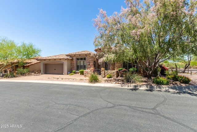 mediterranean / spanish home with a garage, a tiled roof, stucco siding, fence, and stone siding