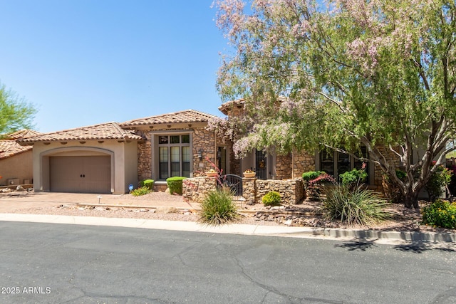 mediterranean / spanish-style house featuring stucco siding, a tile roof, a garage, stone siding, and concrete driveway