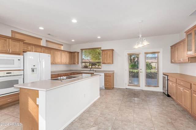 kitchen featuring white appliances, a wealth of natural light, decorative light fixtures, and an island with sink