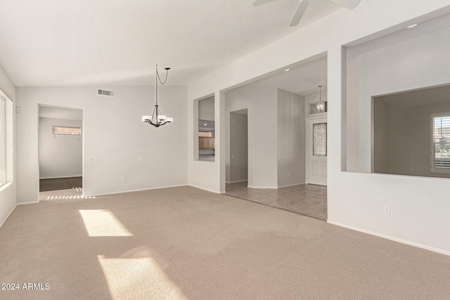 carpeted empty room featuring ceiling fan with notable chandelier and vaulted ceiling