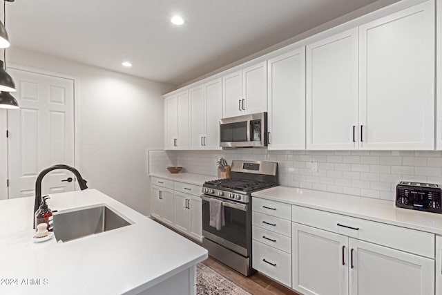 kitchen featuring sink, hanging light fixtures, hardwood / wood-style flooring, white cabinetry, and stainless steel appliances