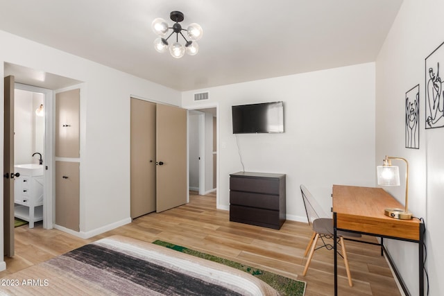 bedroom with light wood-style flooring, baseboards, a chandelier, ensuite bath, and a desk