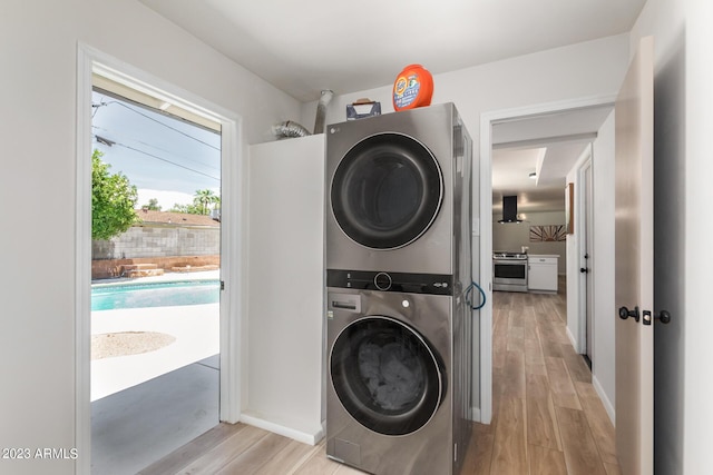 laundry area featuring stacked washer / drying machine, light wood-style flooring, and baseboards