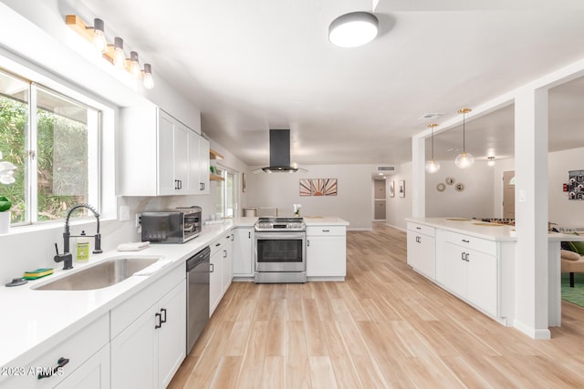kitchen with appliances with stainless steel finishes, a peninsula, island range hood, a sink, and light wood-type flooring