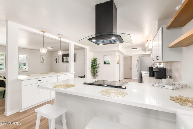 kitchen featuring a peninsula, island exhaust hood, cooktop, and light countertops