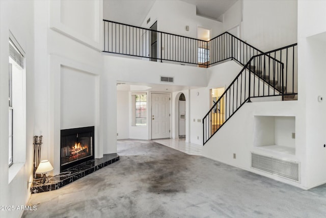 unfurnished living room with light colored carpet, a tile fireplace, and a high ceiling