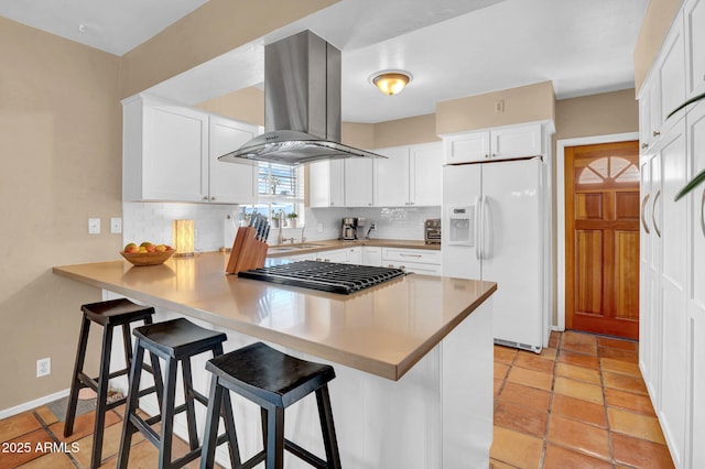 kitchen featuring a peninsula, island exhaust hood, white cabinets, white refrigerator with ice dispenser, and tasteful backsplash