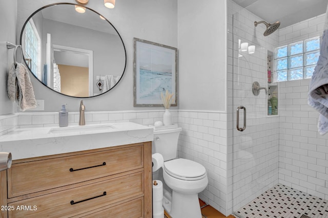 bathroom with vanity, a shower stall, wainscoting, tile walls, and toilet