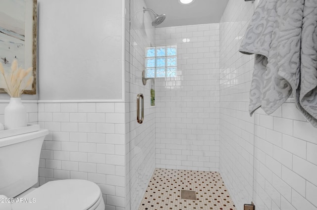 bathroom with a wainscoted wall, a stall shower, toilet, and tile walls