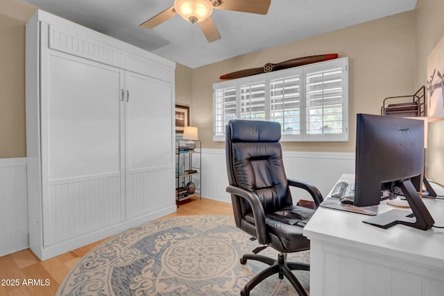 office with light wood finished floors, wainscoting, and a ceiling fan