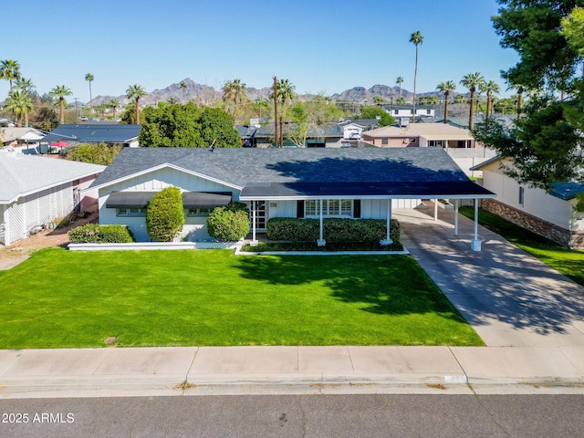 view of front of home featuring an attached carport, a shingled roof, a front yard, driveway, and a mountain view