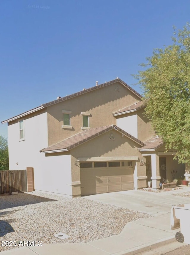 view of front of home with stucco siding, driveway, a garage, fence, and a tiled roof