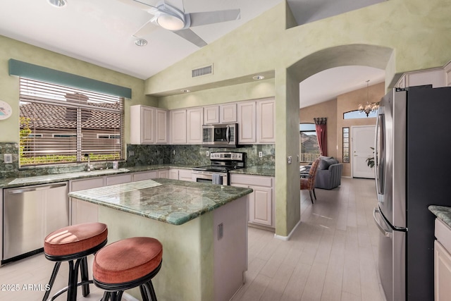 kitchen featuring appliances with stainless steel finishes, dark stone countertops, a center island, a kitchen bar, and vaulted ceiling