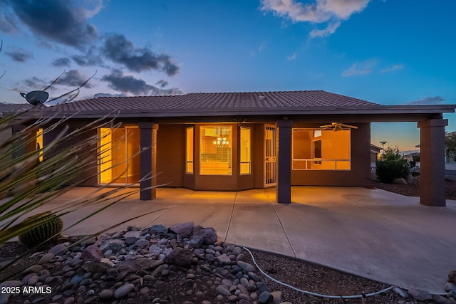 back house at dusk with ceiling fan and a patio