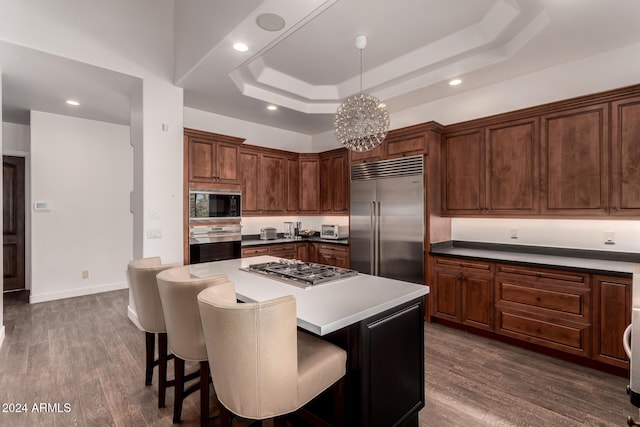 kitchen with a center island, a raised ceiling, built in appliances, a notable chandelier, and dark hardwood / wood-style flooring