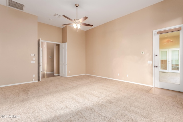 carpeted empty room featuring ceiling fan and a towering ceiling