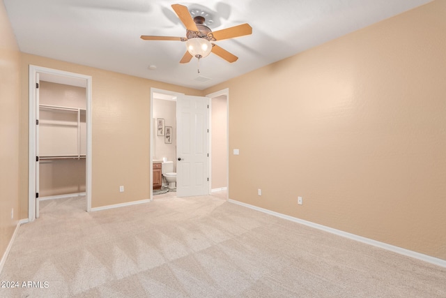 unfurnished bedroom with a closet, connected bathroom, light colored carpet, ceiling fan, and a walk in closet