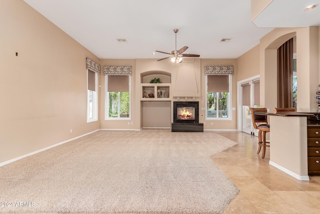 unfurnished living room with built in features, plenty of natural light, ceiling fan, and light tile floors