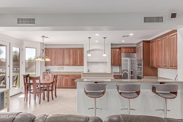 kitchen with visible vents, a peninsula, light stone counters, and stainless steel appliances