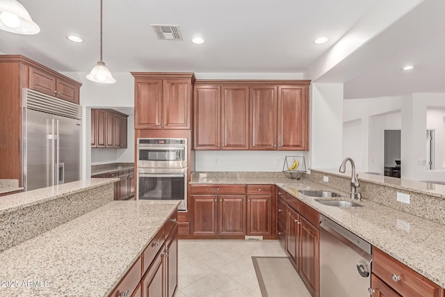 kitchen with visible vents, light stone countertops, a sink, hanging light fixtures, and stainless steel appliances