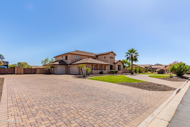 mediterranean / spanish-style home featuring a garage, decorative driveway, fence, a front lawn, and stucco siding
