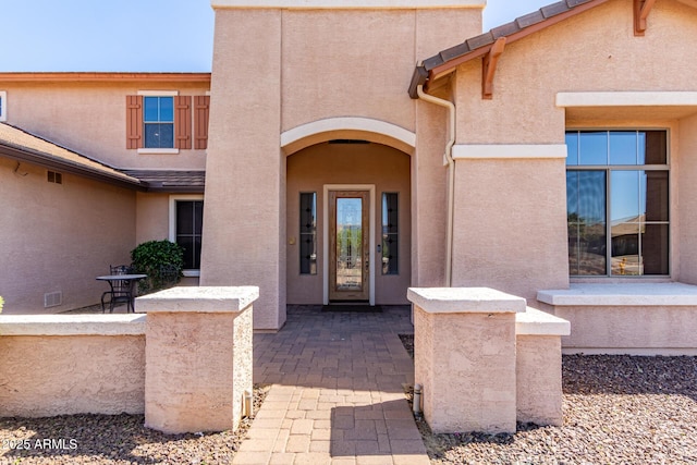 entrance to property with a patio area, visible vents, and stucco siding