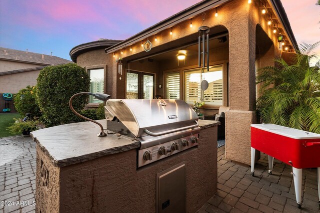 patio terrace at dusk with area for grilling and an outdoor kitchen