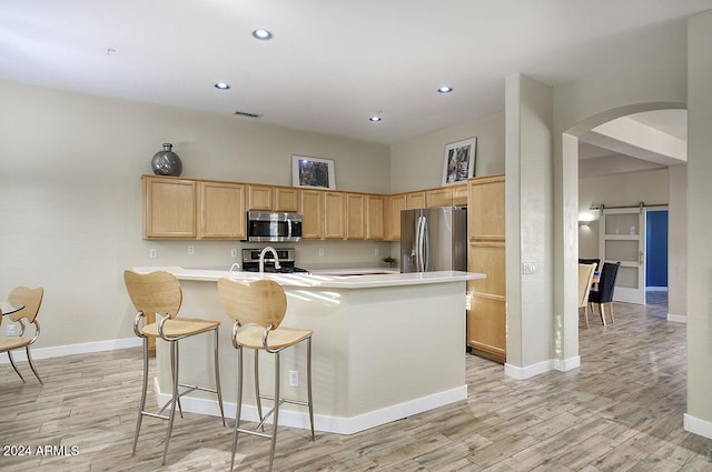14430 N Agave Dr, Fountain Hills, AZ 85268 - kitchen with a barn door, light brown cabinetry, appliances with stainless steel finishes, a center island with sink, and light wood-type flooring