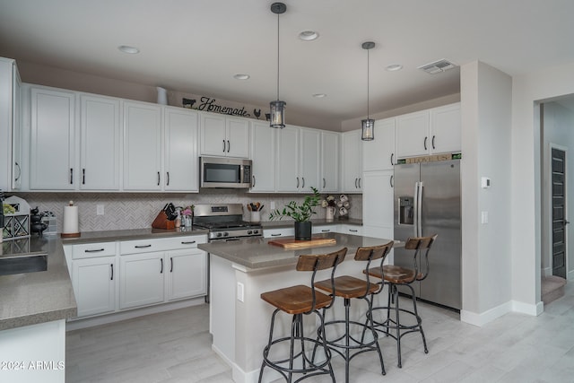 kitchen with decorative backsplash, appliances with stainless steel finishes, decorative light fixtures, and white cabinetry