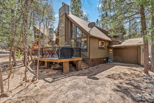 back of property with dirt driveway, an attached garage, a chimney, a shingled roof, and a deck