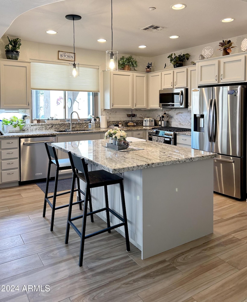 kitchen with white cabinetry, stainless steel appliances, a kitchen island, light stone counters, and sink