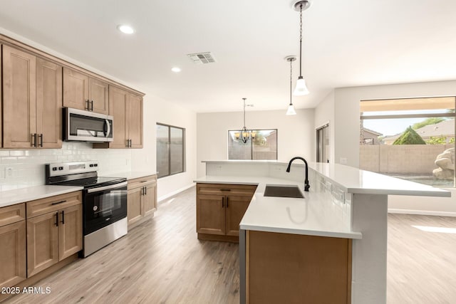 kitchen with appliances with stainless steel finishes, a kitchen island with sink, sink, decorative light fixtures, and a notable chandelier