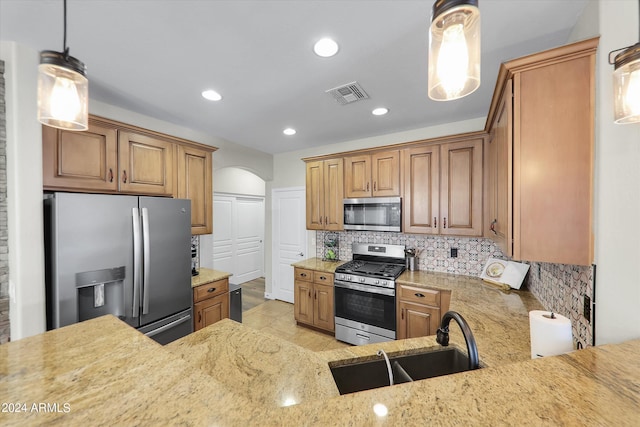 kitchen with light stone counters, decorative backsplash, stainless steel appliances, sink, and pendant lighting