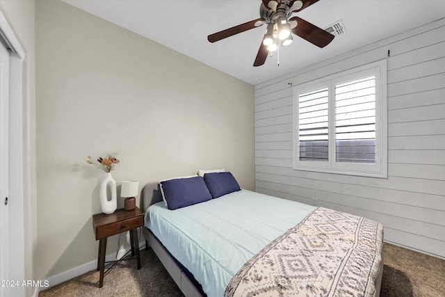 carpeted bedroom featuring ceiling fan, wood walls, and a closet