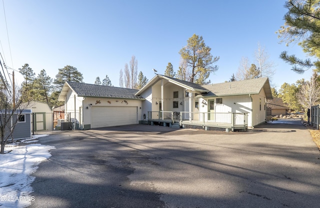 view of front of home featuring aphalt driveway, an attached garage, central AC unit, and fence