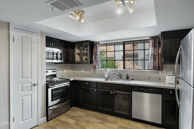 kitchen featuring sink, a tray ceiling, stainless steel appliances, light stone countertops, and light wood-type flooring