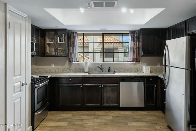 kitchen featuring sink, appliances with stainless steel finishes, dark brown cabinetry, a tray ceiling, and light wood-type flooring